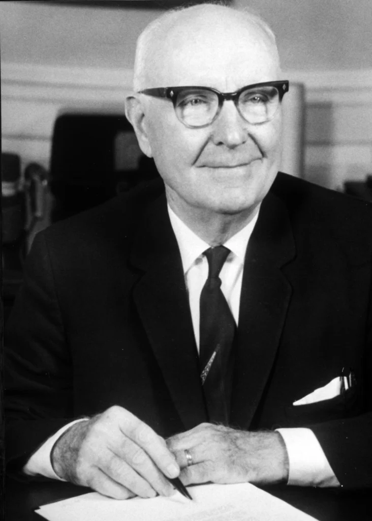 Black and white portrait of a foundation founder seated at a desk holding a pen.