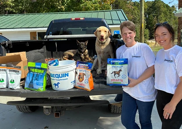 Staff members stand beside a truck loaded with donated equine supplements and supplies supporting the care of therapy horses at Wings of Eagles Ranch.
