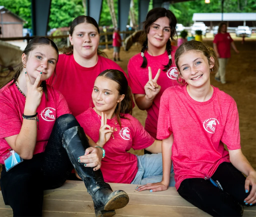 Teen volunteers from Wings of Eagles Ranch smile together in the riding arena after helping with therapeutic riding activities.